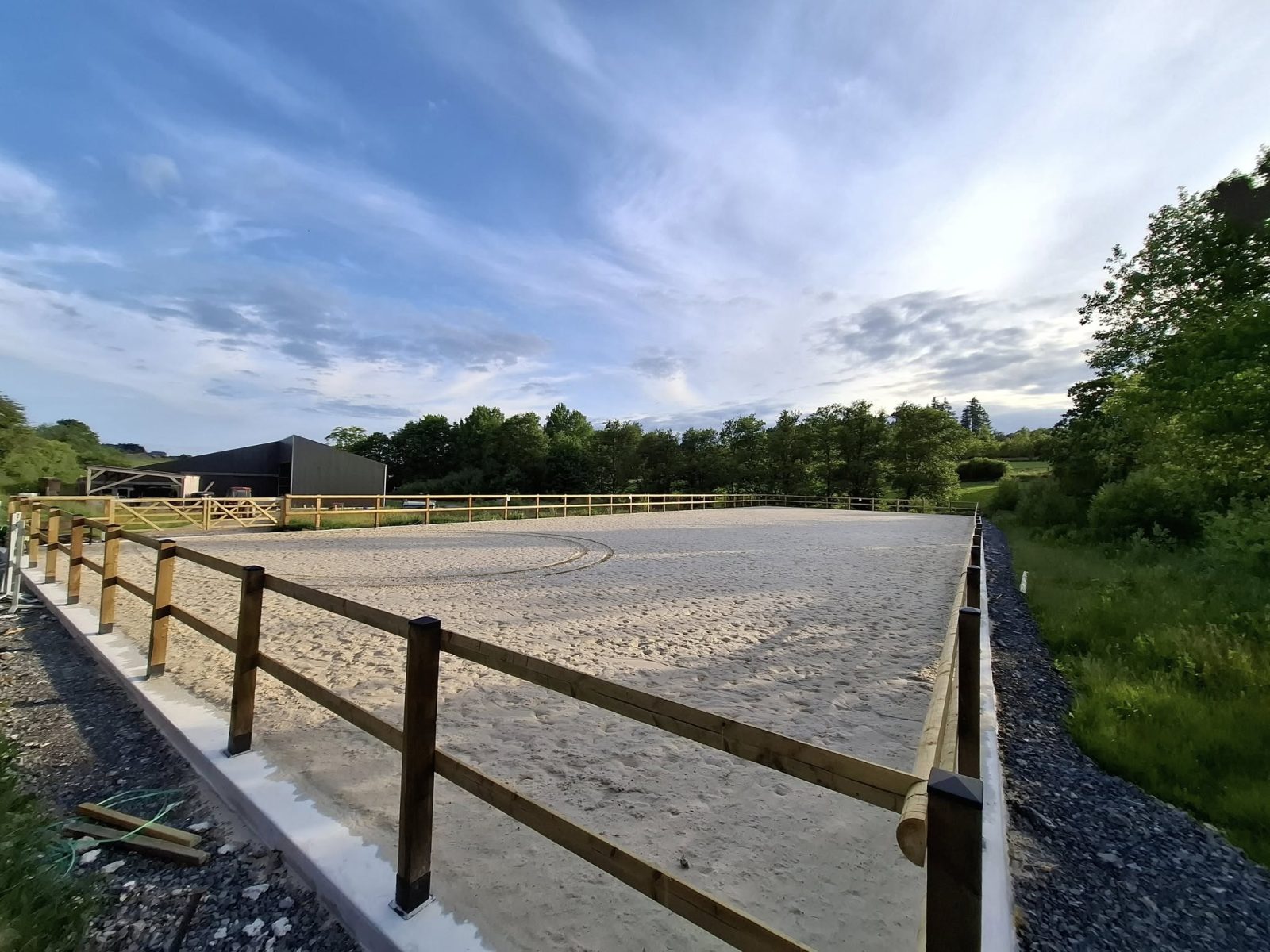 La piste extérieure de l'Écurie de la Tannerie en fin de journée, entourée de prairies et de bois
