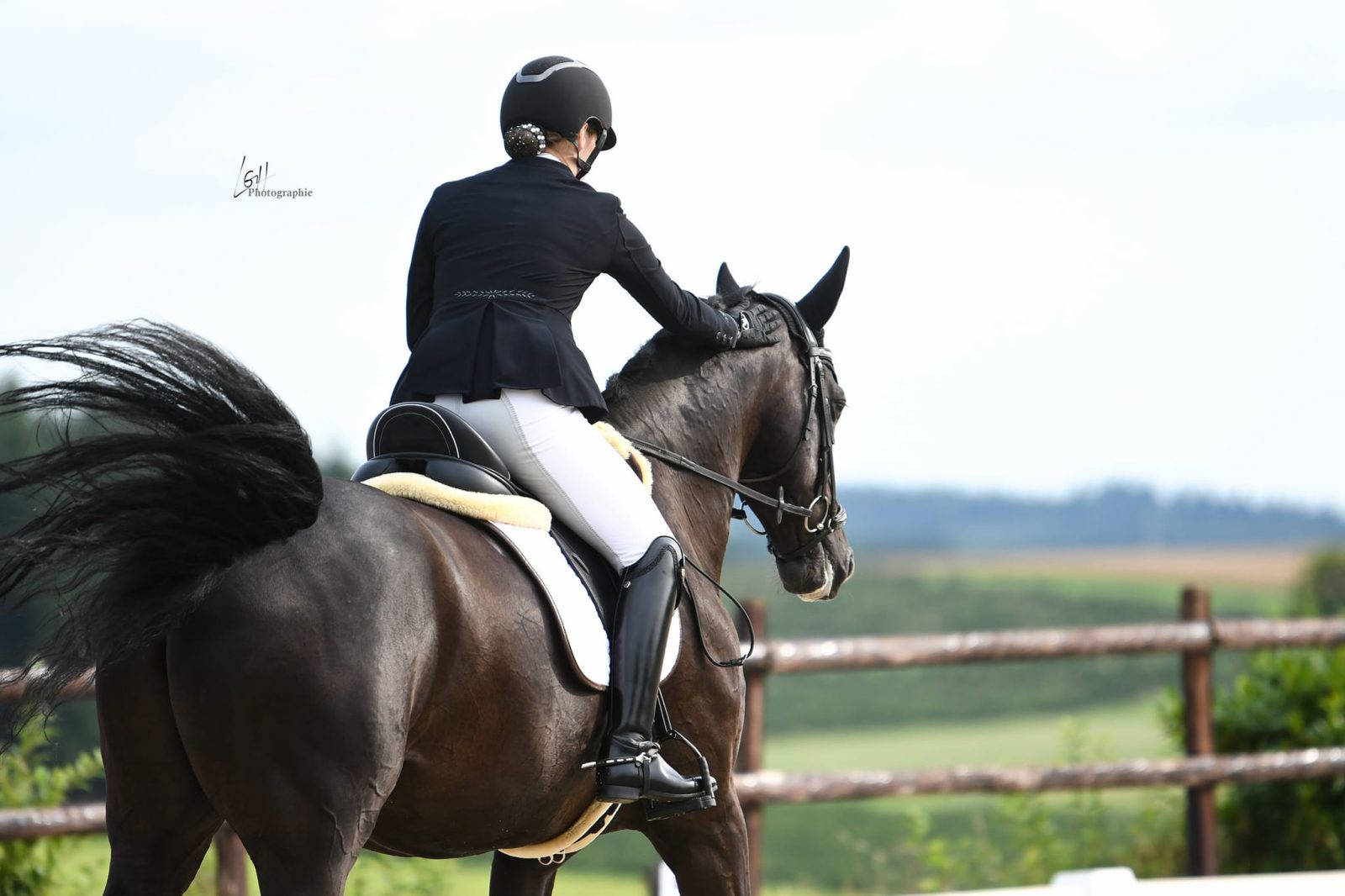 Cavalière en tenue de concours à cheval, face aux prairies