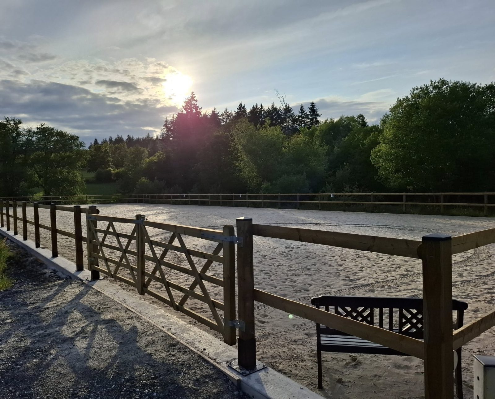 La piste extérieure en sable clair au soleil couchant, sa clôture en bois et son banc d'observation